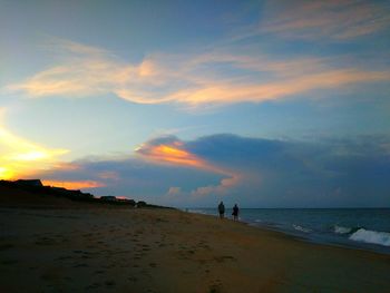 Silhouette people on beach against sky during sunset