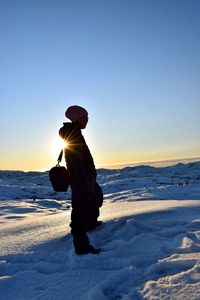 Woman standing on snow against sky during sunset