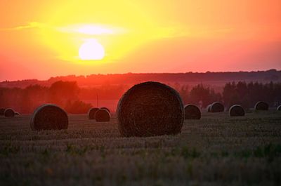 Hay bales on field against sky during sunset