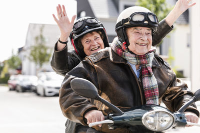 Happy senior couple having fun, riding motor scooter and waving