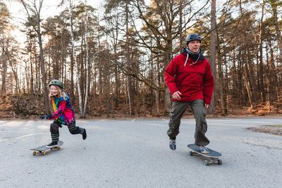 Carefree father and daughter in helmets riding skateboards in park and having fun together during weekend