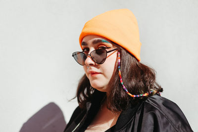 Serious young female with colorful makeup in colorful hat and sunglasses with beaded chain looking at camera on white background