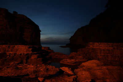 Rock formations by sea against sky at dusk