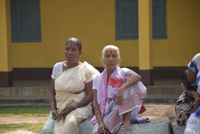 Women wearing saris sitting against built structure
