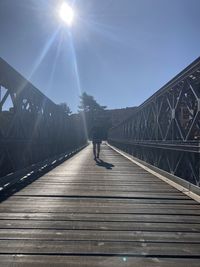Man walking on footbridge against sky