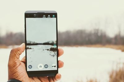 Close-up of hand holding smart phone against sky