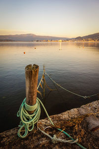 Rope tied to wooden post in lake against sky