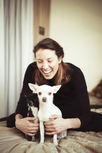 Young woman laughs at home with two chihuahua dogs in warm light