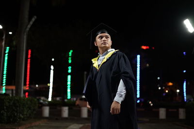 Young man wearing graduation gown at night