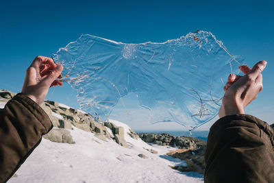 Cropped image of person holding ice on snow field against clear sky
