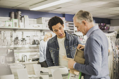 Mature salesman showing appliance to male customer in store