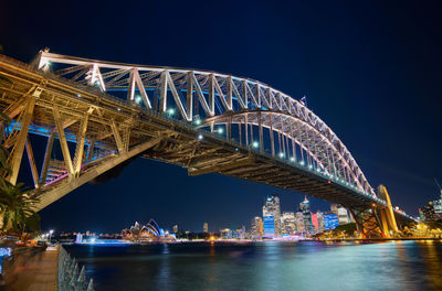 Sydney harbor bridge over parramatta river against sky in city at night