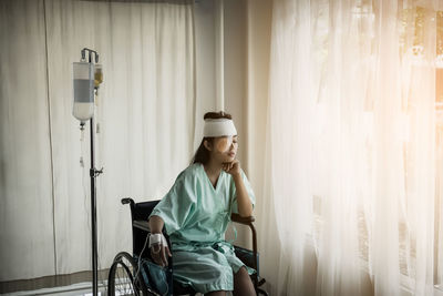 Woman with physical injury sitting on wheelchair by iv drip at hospital
