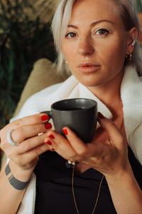 Close up of blond woman holding cup of coffee while looking at camera