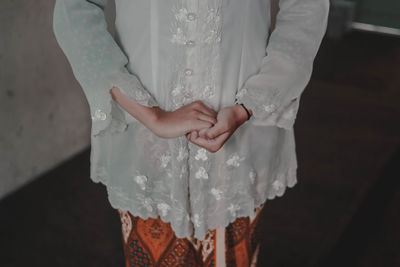 Midsection of woman with hands clasped standing on floor