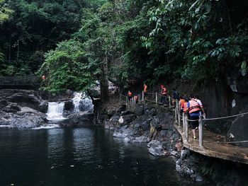 People on bridge leading towards waterfall in forest