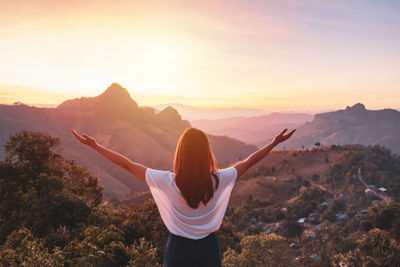 Rear view of woman standing on mountain during sunset