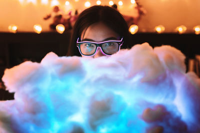 Woman holding illuminated cloud while sitting on bed at home