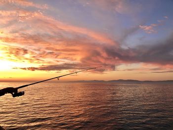 Silhouette fishing rod on sea against sky during sunset