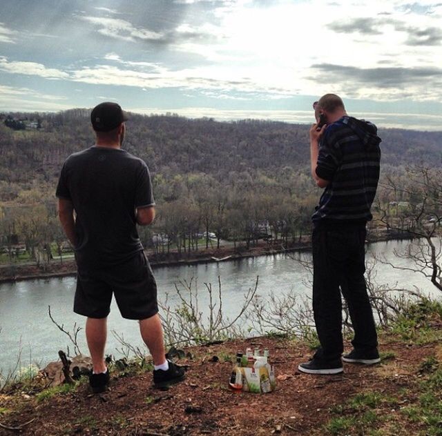 REAR VIEW OF MEN STANDING ON RIVERBANK AGAINST SKY