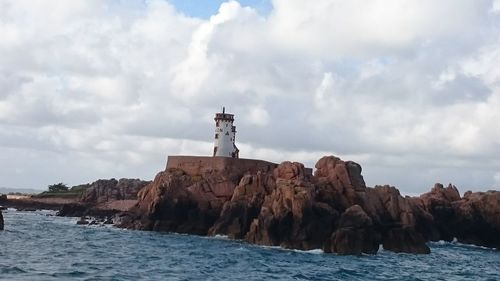 Lighthouse on rock by sea against buildings