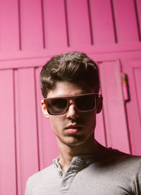 Portrait of young man wearing sunglasses against pink wall