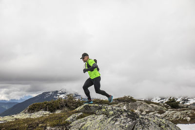 Side view of fit active man trail running on mountain ridge.