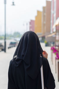 Single muslim woman walks through empty big city, rear view.