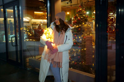 Caucasian white girl near a shop window, with a christmas tree in her hands, garlands are branching