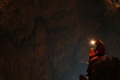 Side view of spelunker wearing illuminated headlamp in cave