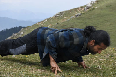 A handsome long haired indian young man doing push-ups with three fingers in the top of mountain