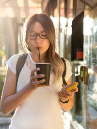 Woman drinks cappuccino with straw. cup of take away coffee. street life in town.