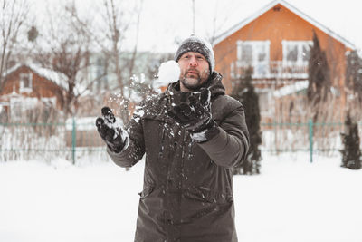 A man throws snowballs in the yard of a private house on a frosty day, snow games in the air.