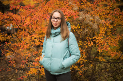 Portrait of young woman standing by autumn tree