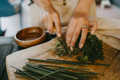 Hands of female chef chopping leafy vegetable on cutting board in studio