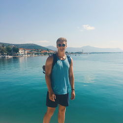 Portrait of smiling young man standing by sea against sky