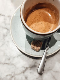 A cup of espresso with a lump of brown sugar on top of a marble table.