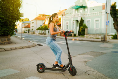 Young woman standing on electric push scooter on street