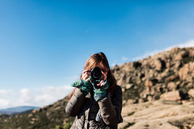 Portrait of woman photographing against blue sky