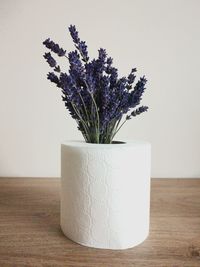 Close-up of flowers in toilet paper roll on table against wall