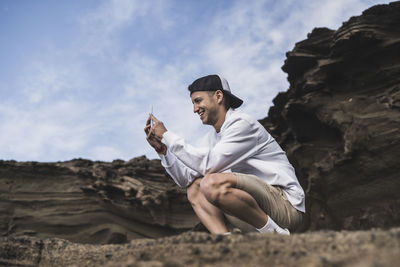 Man sitting on rock against sky