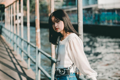 Portrait of young woman standing against railing