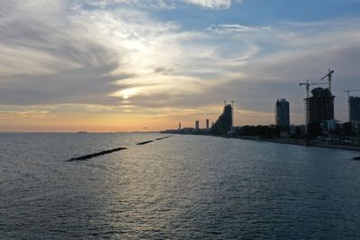 Sea by buildings against sky during sunset