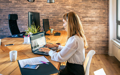 Woman with headset typing in laptop in customer help service