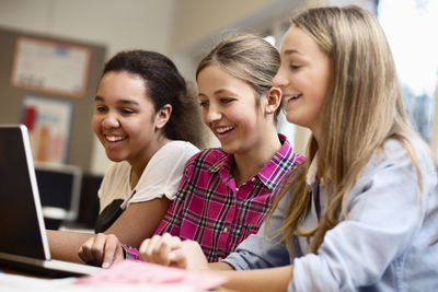 Happy schoolgirls using laptop together in classroom