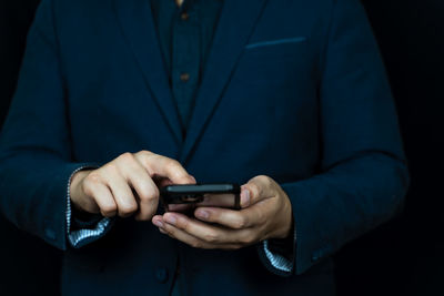 Midsection of man using mobile phone against black background