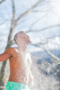 Midsection of shirtless boy/man standing outside on a cold snowy day. snow splash