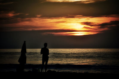 Silhouette people standing on beach against sky during sunset