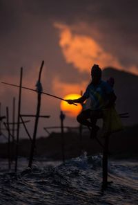 Silhouette people standing by sea against sky during sunset