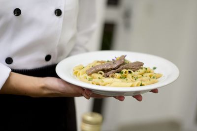 Midsection of female chef holding pasta in kitchen